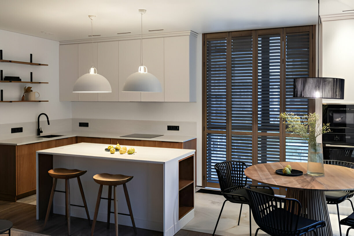 Contemporary kitchen with white cabinets, wood accents, pendant lighting, an island with bar seating, and a dining area with a round wooden table and black chairs