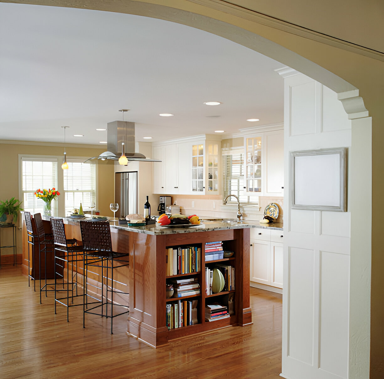 Spacious open-concept kitchen with white cabinets, wood island, built-in bookshelves, pendant lights, and stainless-steel appliances