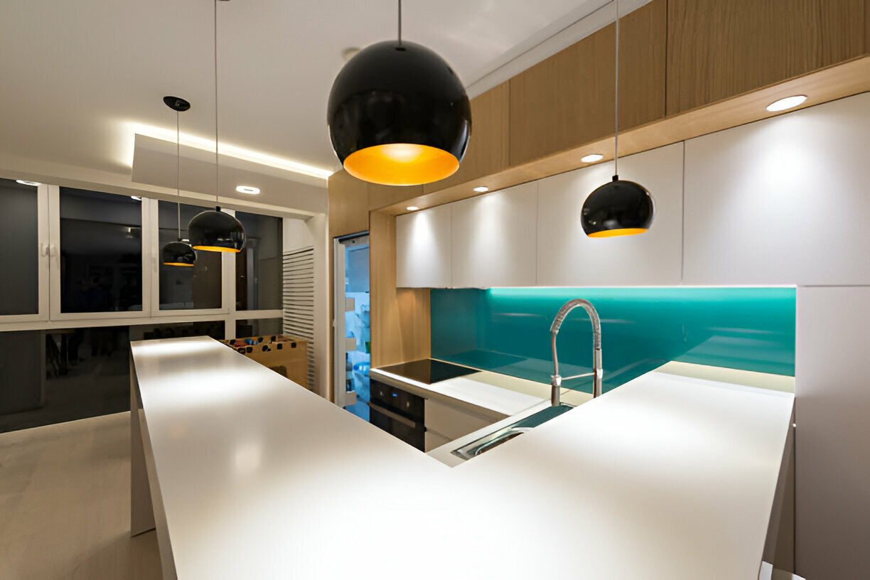 Modern U-shaped kitchen with white countertops, wooden upper cabinets, teal glass backsplash, and black pendant lights