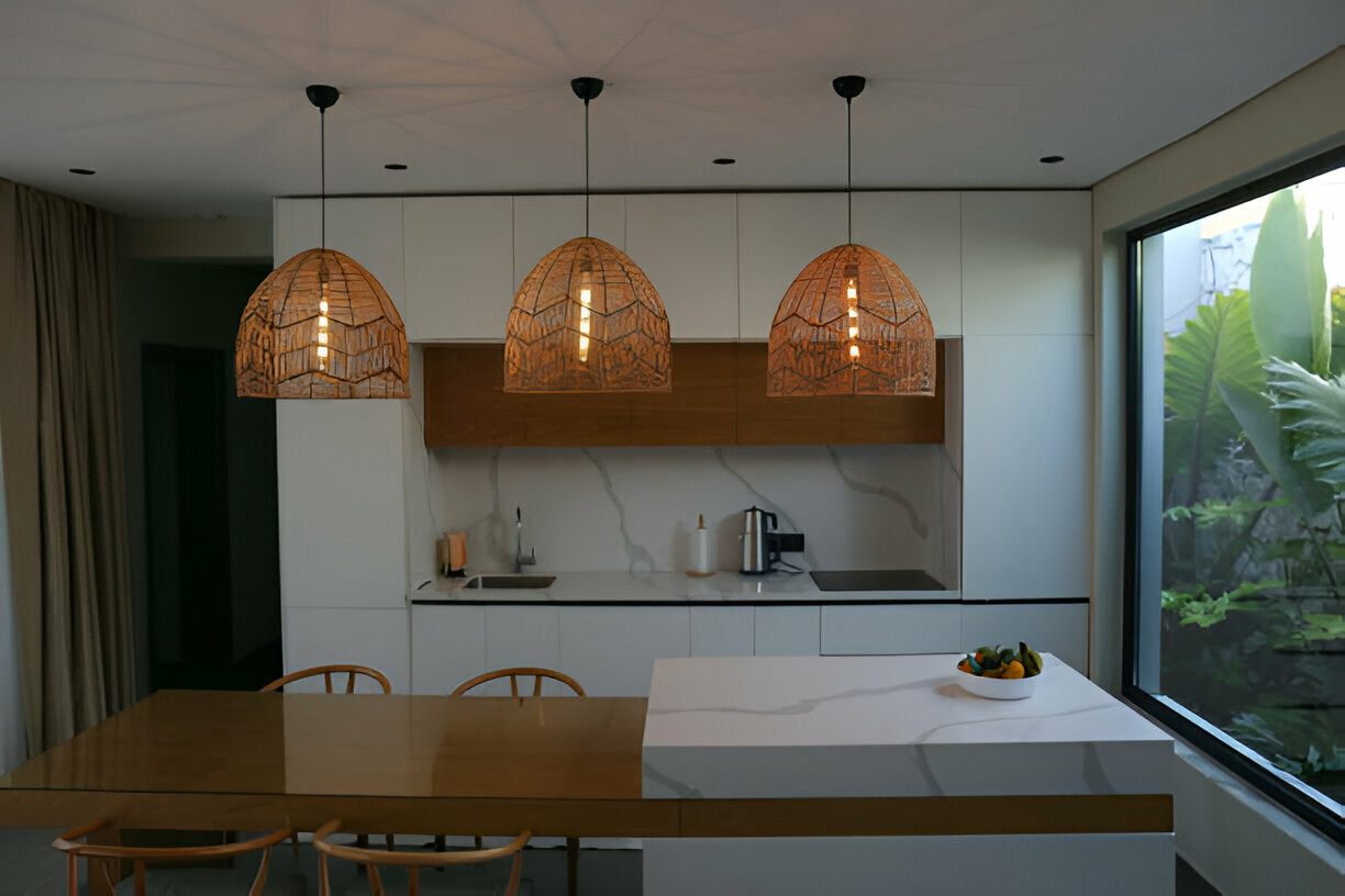 Minimalist kitchen with white and wood cabinetry, marble-effect backsplash, kitchen island, and woven pendant lights. Large window with a garden view