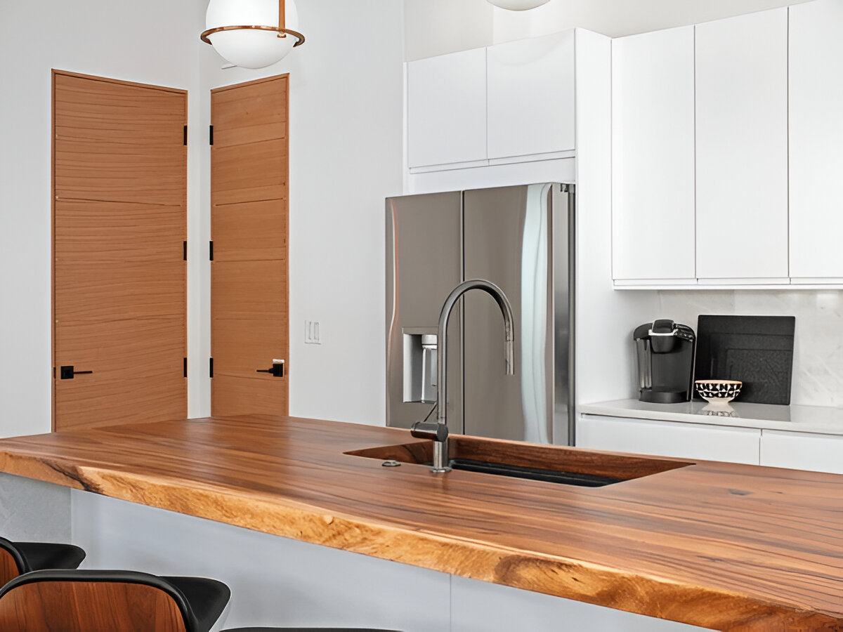 Modern kitchen featuring a natural wood countertop, undermount sink, sleek faucet, white cabinets, stainless steel appliances, and wooden interior doors