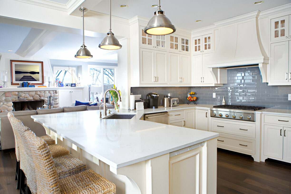Coastal-style kitchen with white cabinets, blue subway tile backsplash, quartz island, stainless steel appliances, and rattan barstools
