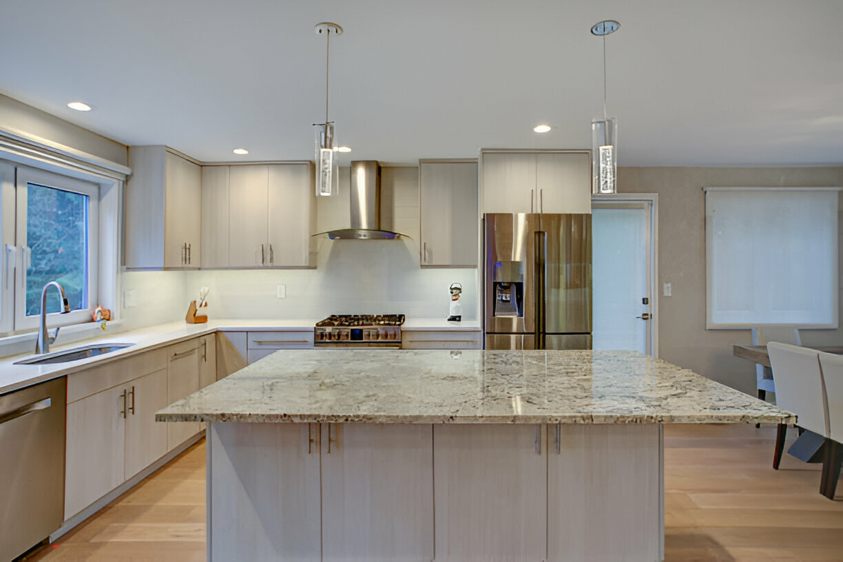 Modern kitchen with light wood cabinets, a large granite island, stainless steel appliances, pendant lighting, and an open floor plan