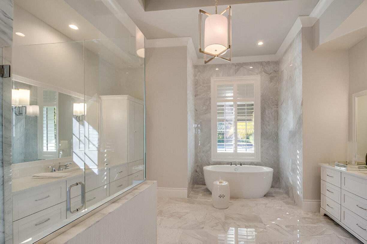 A luxurious bathroom featuring marble flooring, a freestanding bathtub, a glass-enclosed shower, and elegant lighting.
