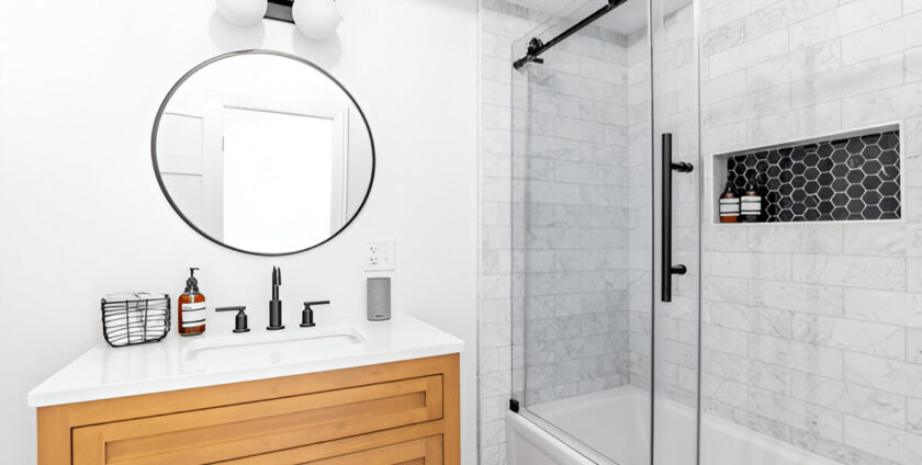 Bathroom interior with wooden vanity, round mirror, and glass shower with black hardware