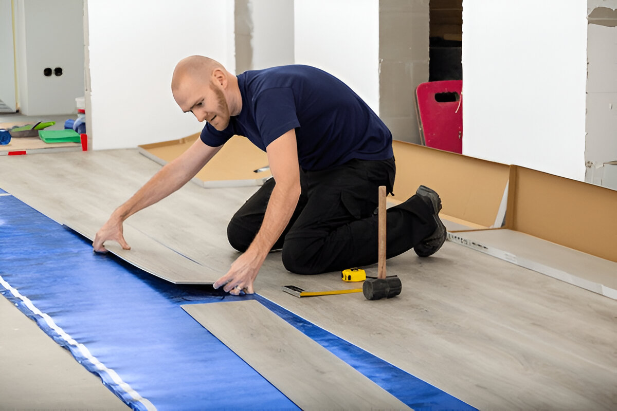 Contractor installing vinyl plank flooring over underlayment in a modern interior