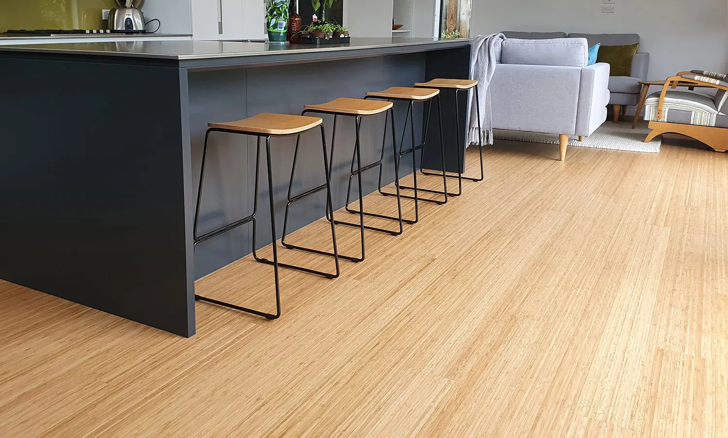 Modern kitchen with light bamboo flooring and black island with wooden bar stools