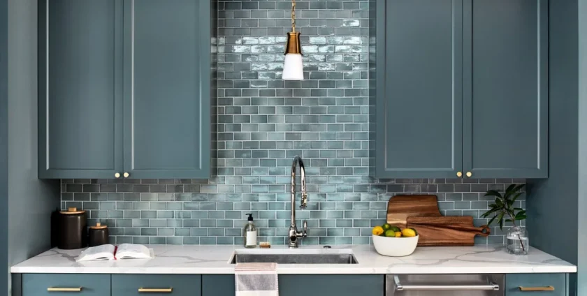Modern kitchen with teal cabinetry, glossy blue subway tile backsplash, brass hardware, and marble countertop.