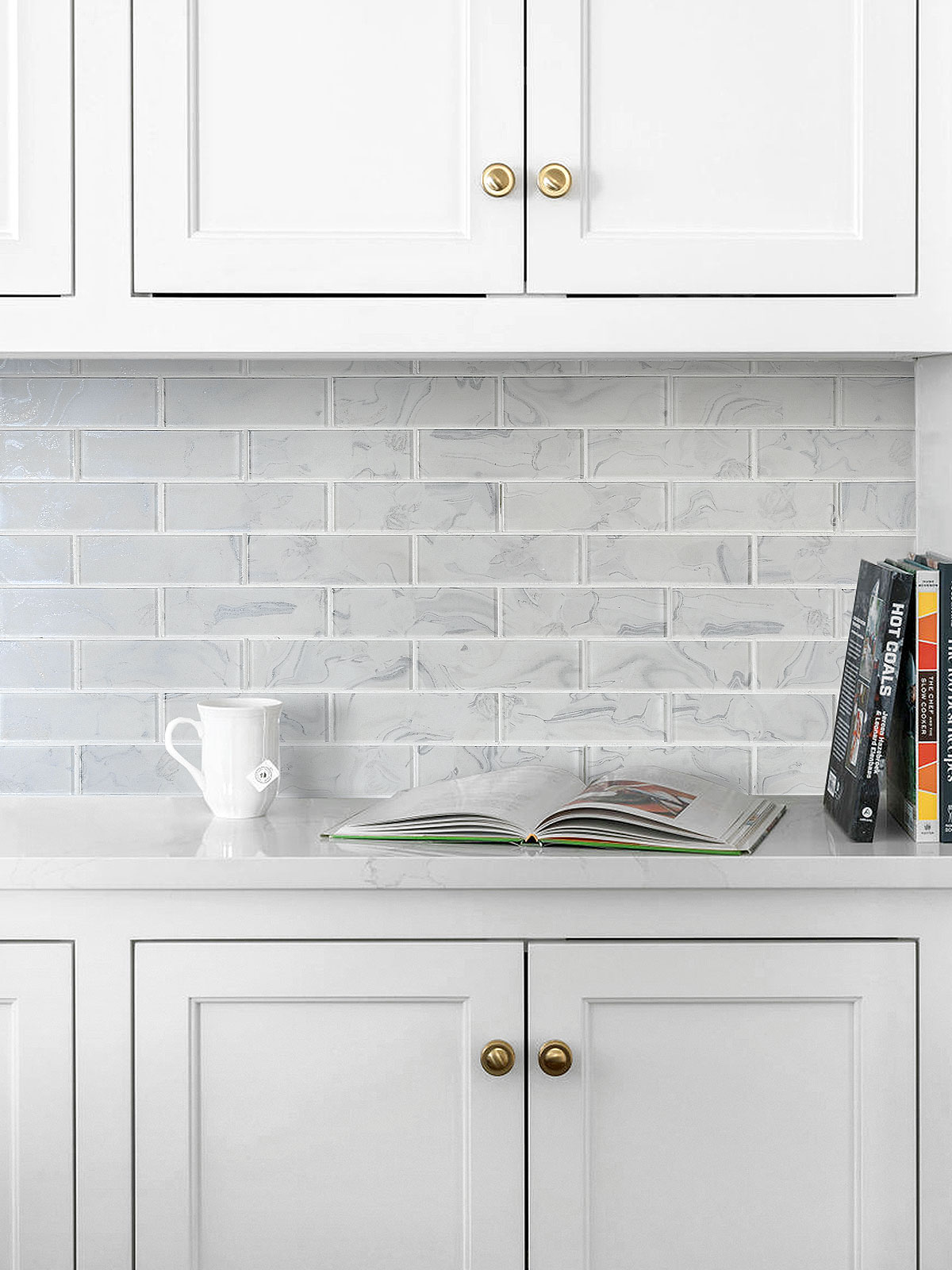 White kitchen with marble-effect glossy subway tile backsplash and brass cabinet knobs.