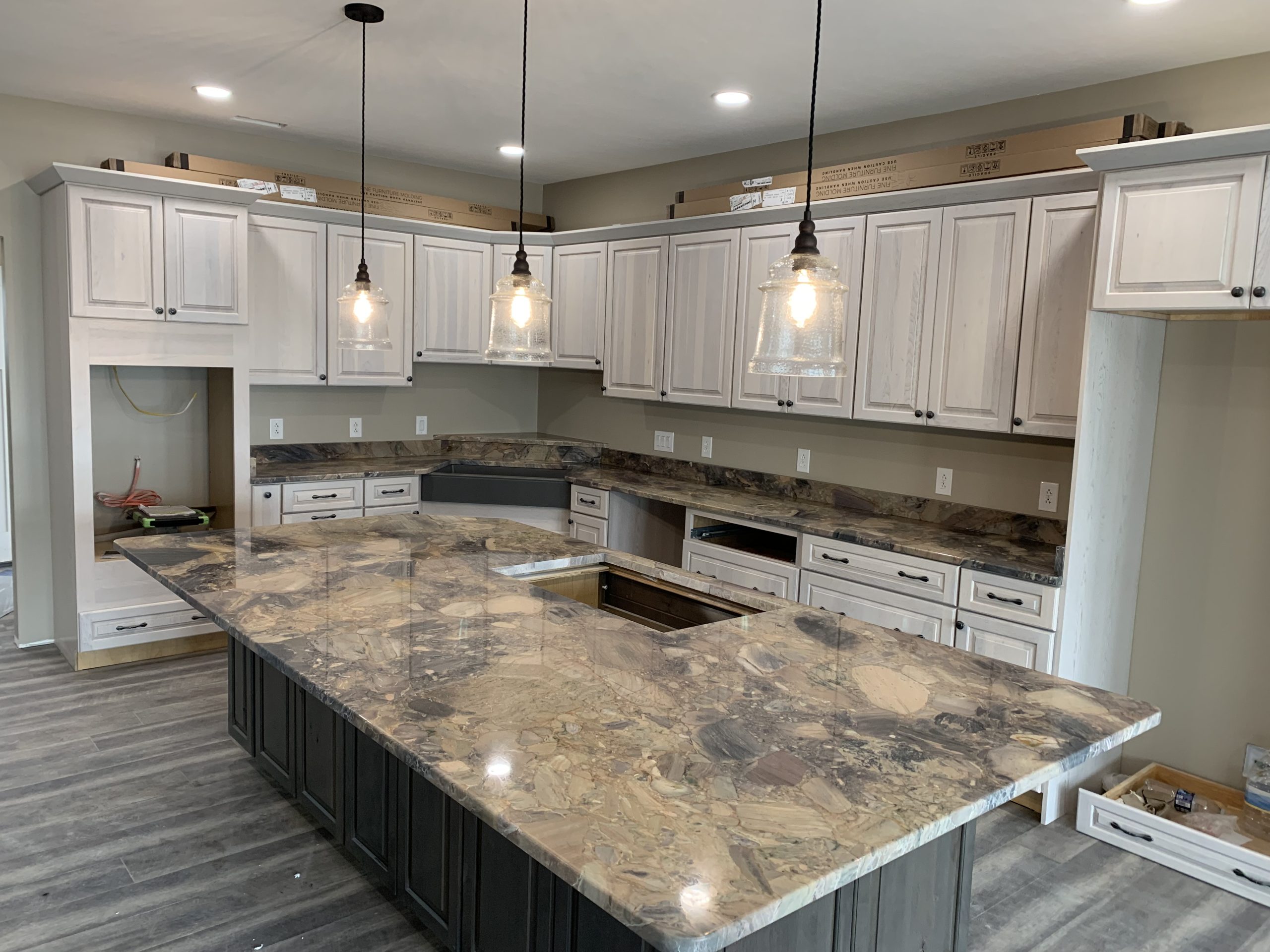 Kitchen with large natural stone island, light wood cabinets, and pendant lighting above the countertop