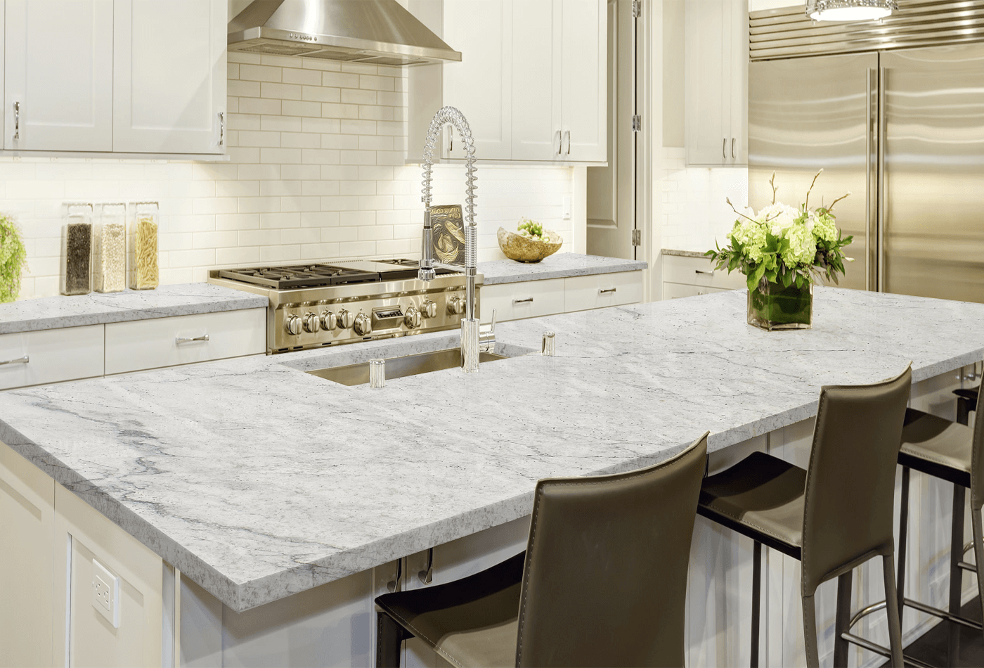 Transitional kitchen featuring light gray granite countertops, stainless steel appliances, white cabinetry, and a central island with sink