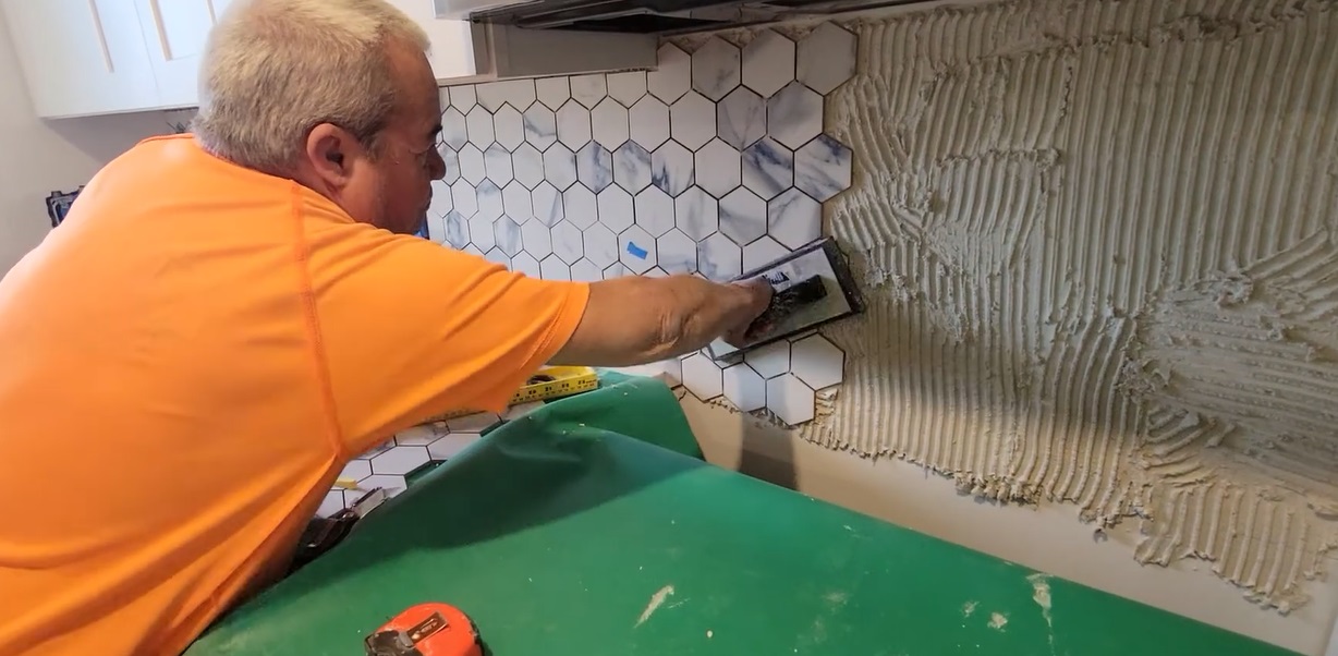 Man installing hexagon marble kitchen backsplash tiles