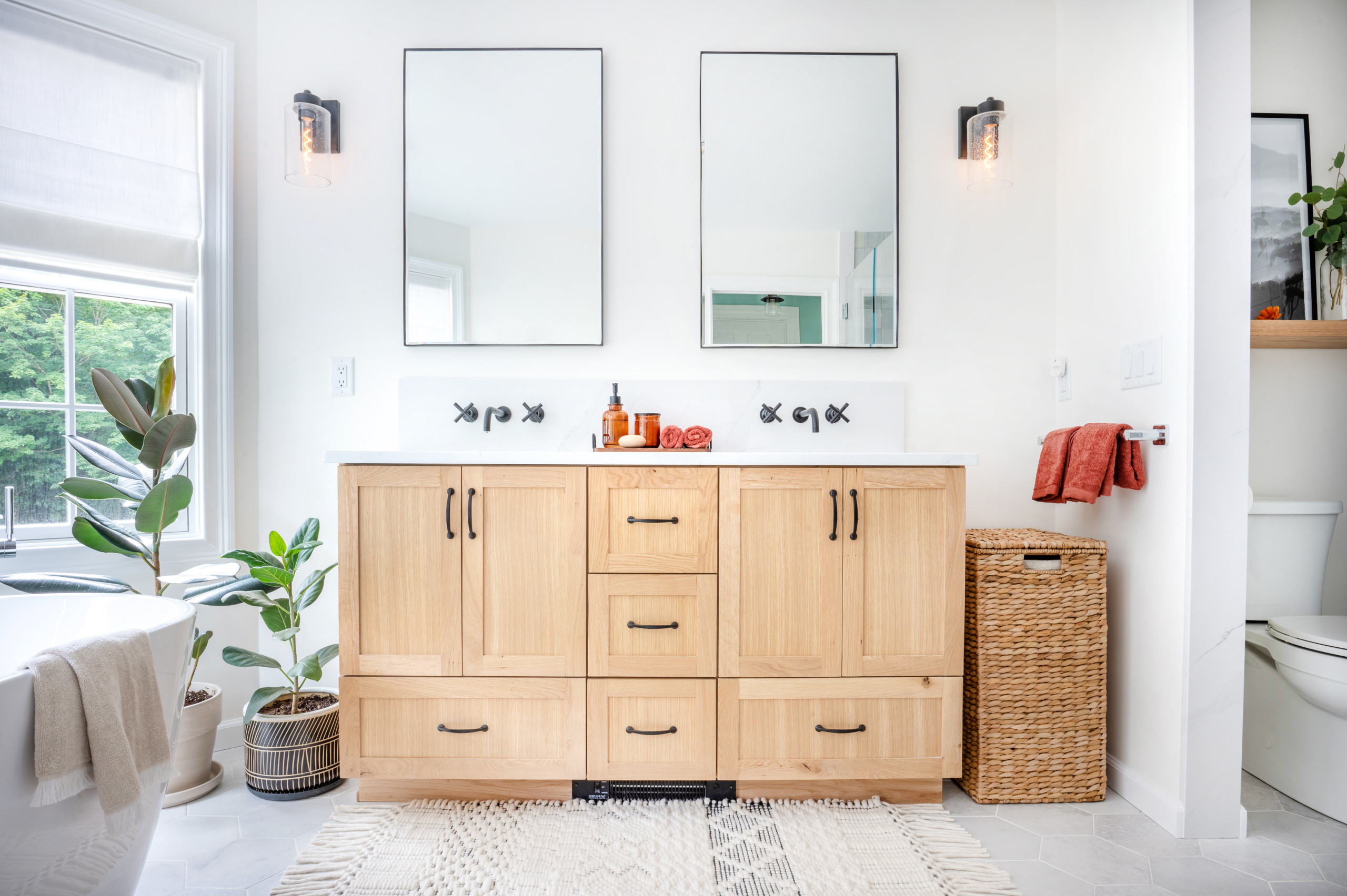 Modern bathroom vanity with light wood cabinets, dual mirrors, and black fixtures