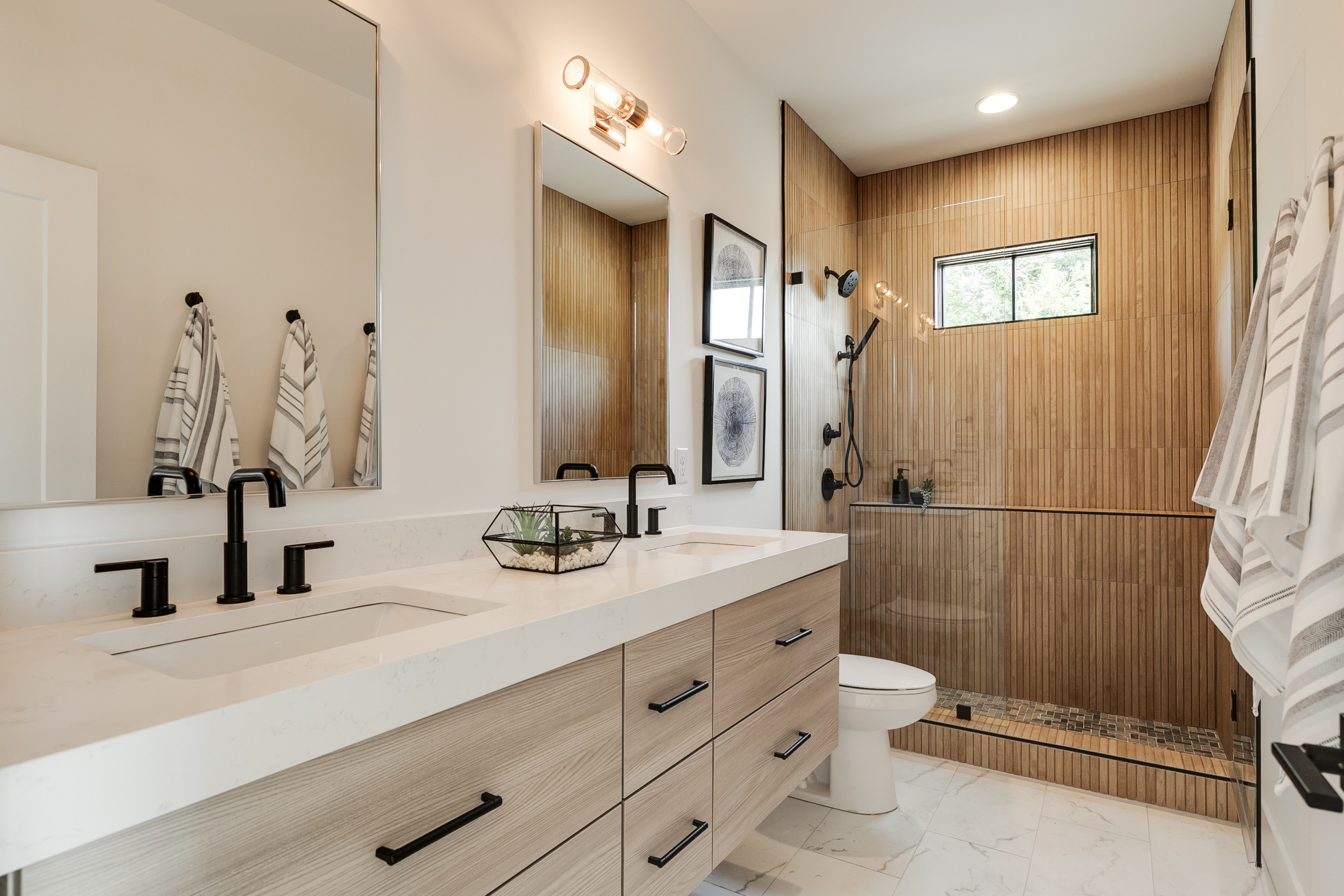 Modern bathroom with wood-accent shower, double vanity, and black fixtures