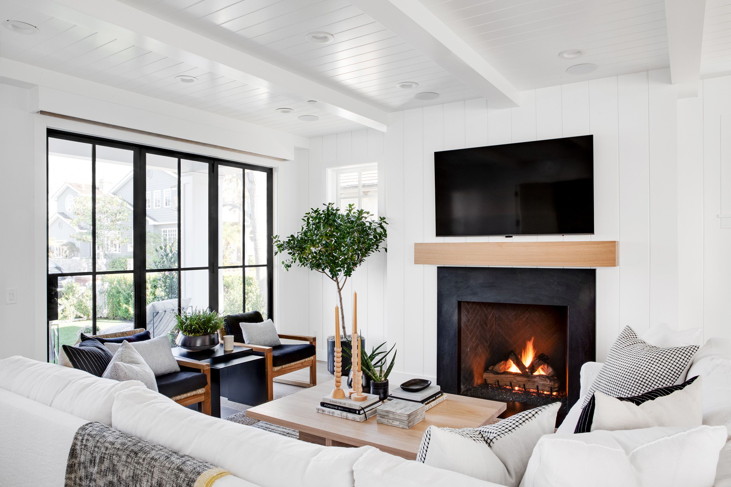 Modern white living room with fireplace, wall-mounted TV, and large windows.
