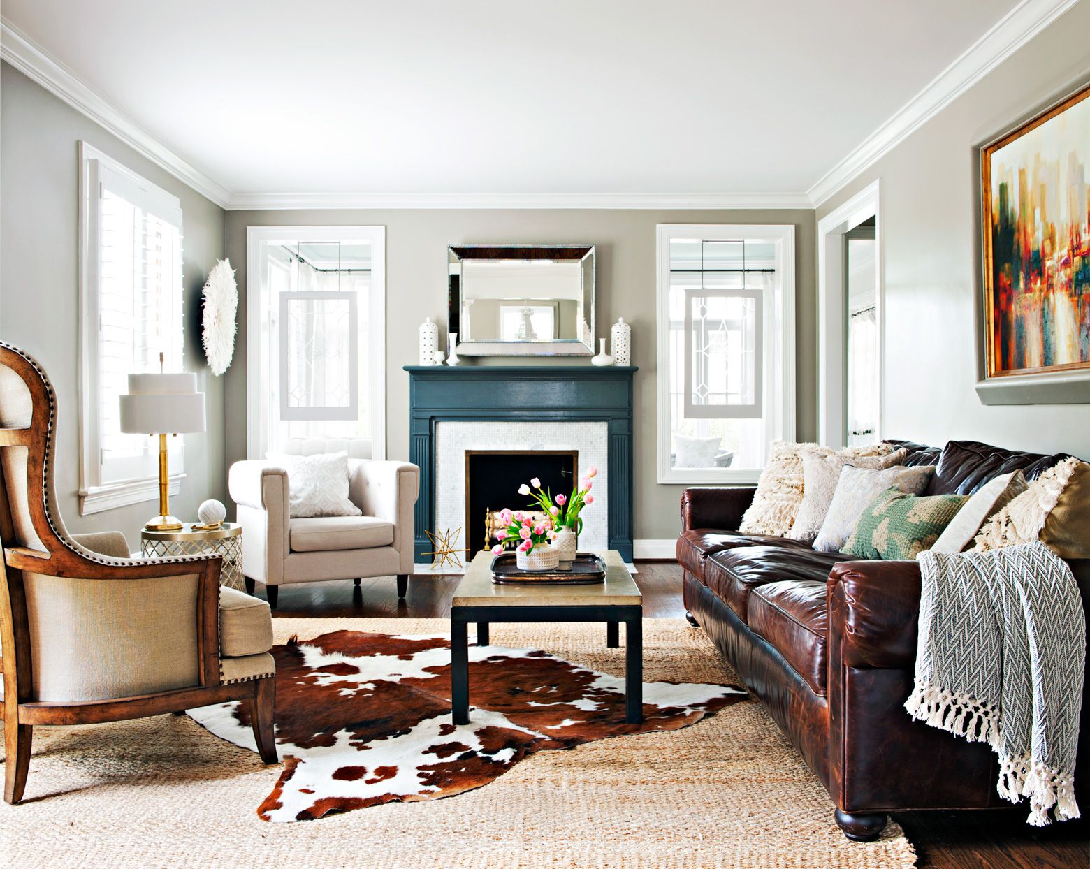 Bright family room with a blue fireplace mantel, brown leather sofa, cowhide rug, and modern neutral decor.