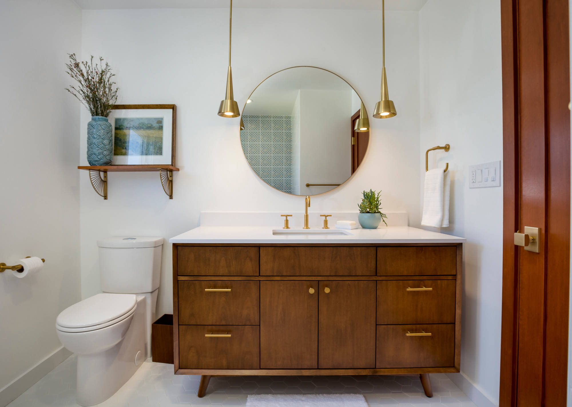 Mid-century modern bathroom with wooden vanity, round mirror, gold fixtures, and minimalist décor.