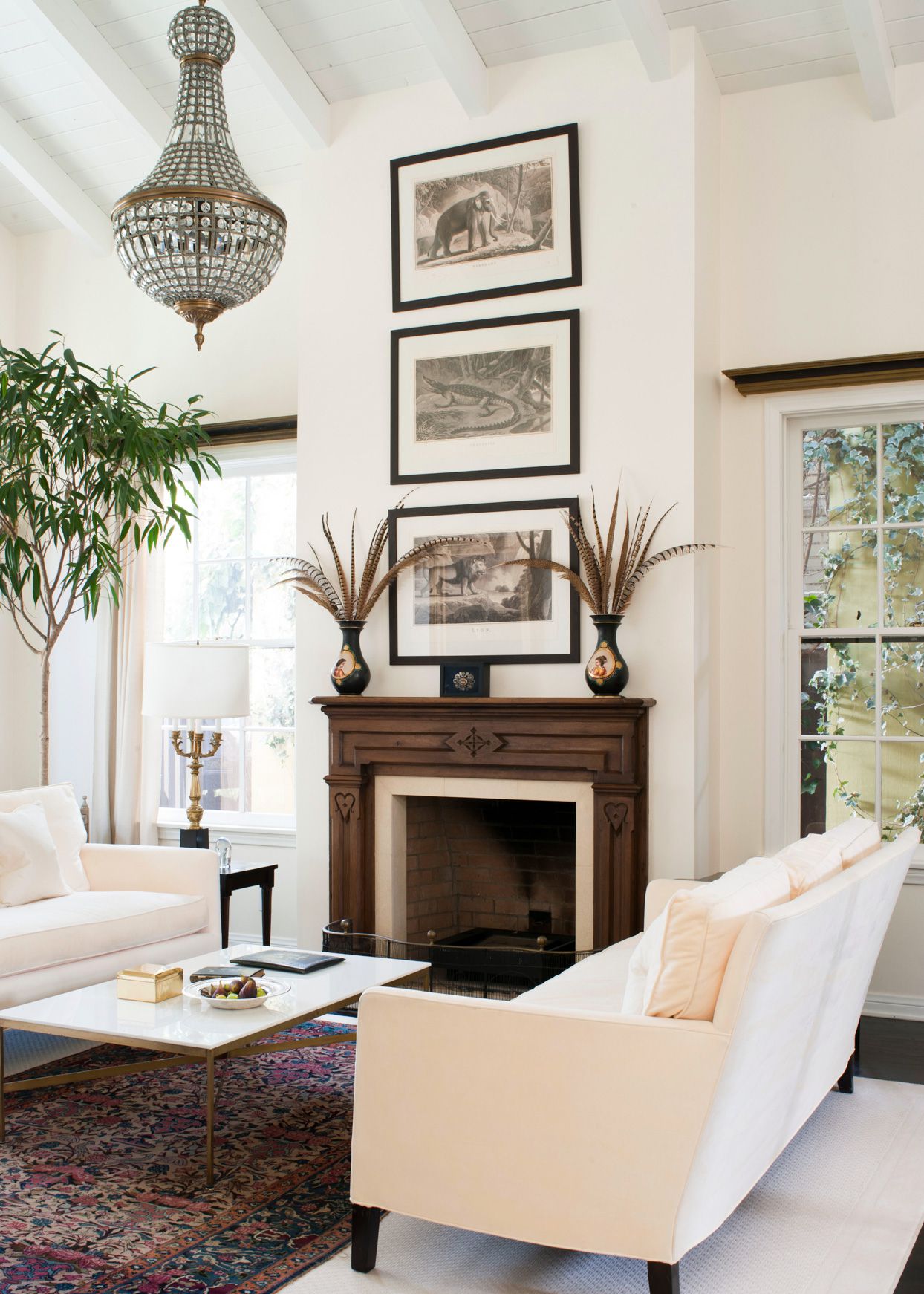 Bright white living room with dark wood fireplace mantel, crystal chandelier, and neutral sofas.